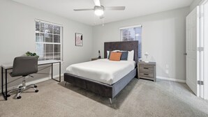 Un dormitorio con cama, escritorio, silla, mesita de noche y ventilador de techo.