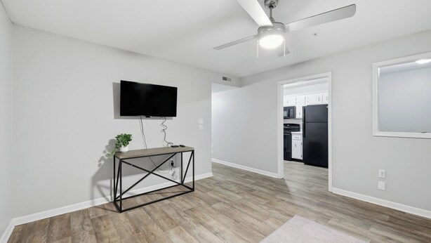 Una sala de estar moderna con un televisor de pantalla plana, un ventilador de techo y una cocina visible al fondo.