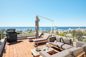 A rooftop terrace with a grill, lounge chairs, a sofa, and a table with drinks. - Elegant Fresnaye Ocean View 4bed Nerine Manor (Cape Town)