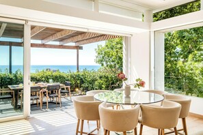 Un área de comedor exterior moderna con una mesa y sillas de vidrio, con vista a un paisaje marino.