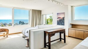 A modern hotel room with a large window offering a city view, a cozy seating area, and a wooden side table. - Elegant Fresnaye Ocean View 4bed Nerine Manor (Cape Town)