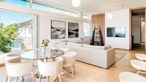 A modern living room with a glass dining table, white sofas, and a large TV. - Elegant Fresnaye Ocean View 4bed Nerine Manor (Cape Town)