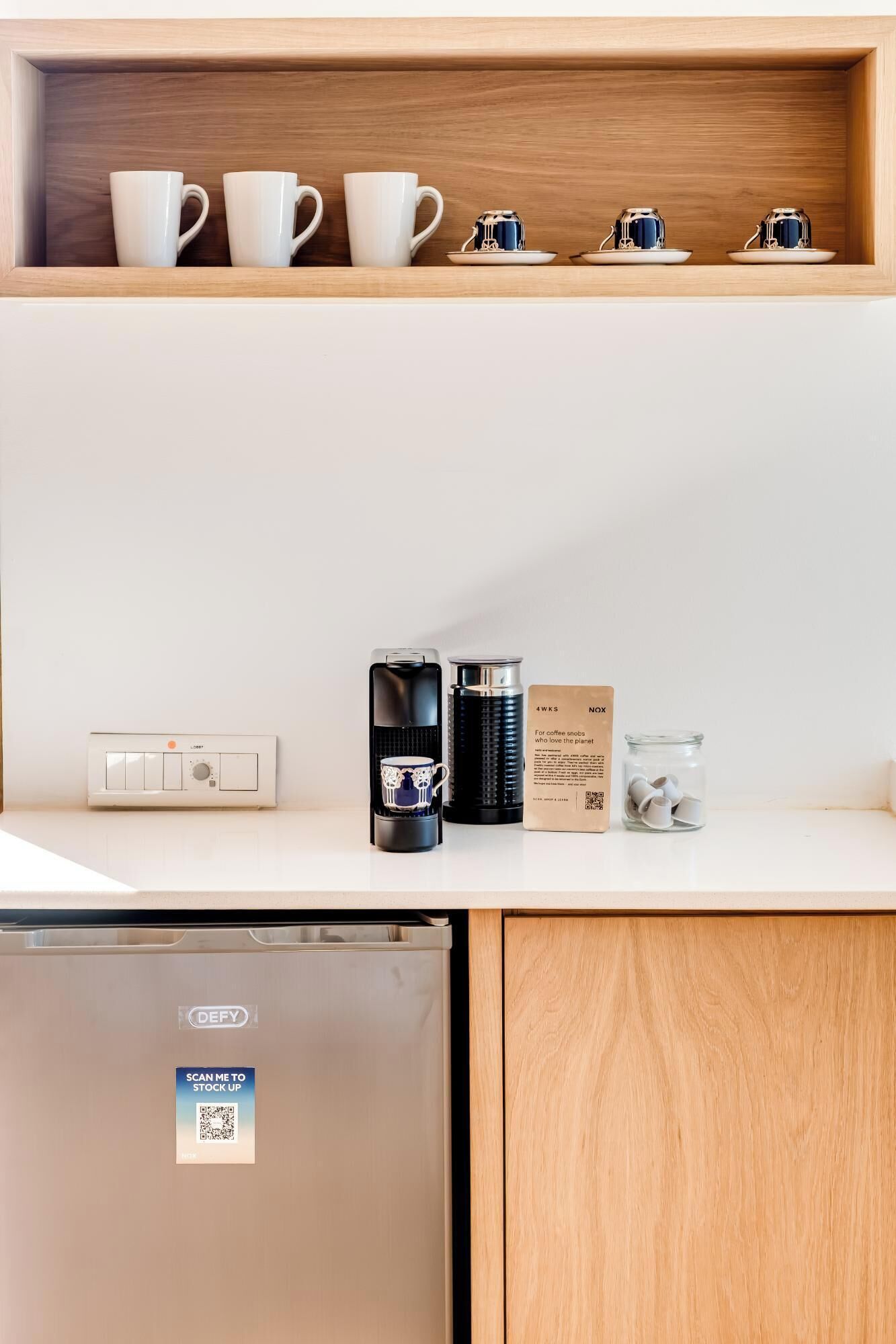 A kitchenette with a coffee maker, a box labeled "4WKS NOX," and a jar of coffee pods.