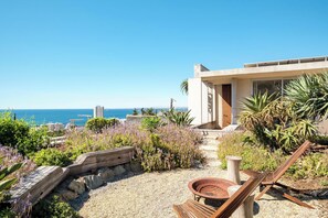 A modern outdoor patio with a seating area, a fire pit, and a view of the ocean. - Opulent Spacious Fresnaye Sea View Leonotis Villa (Cape Town)