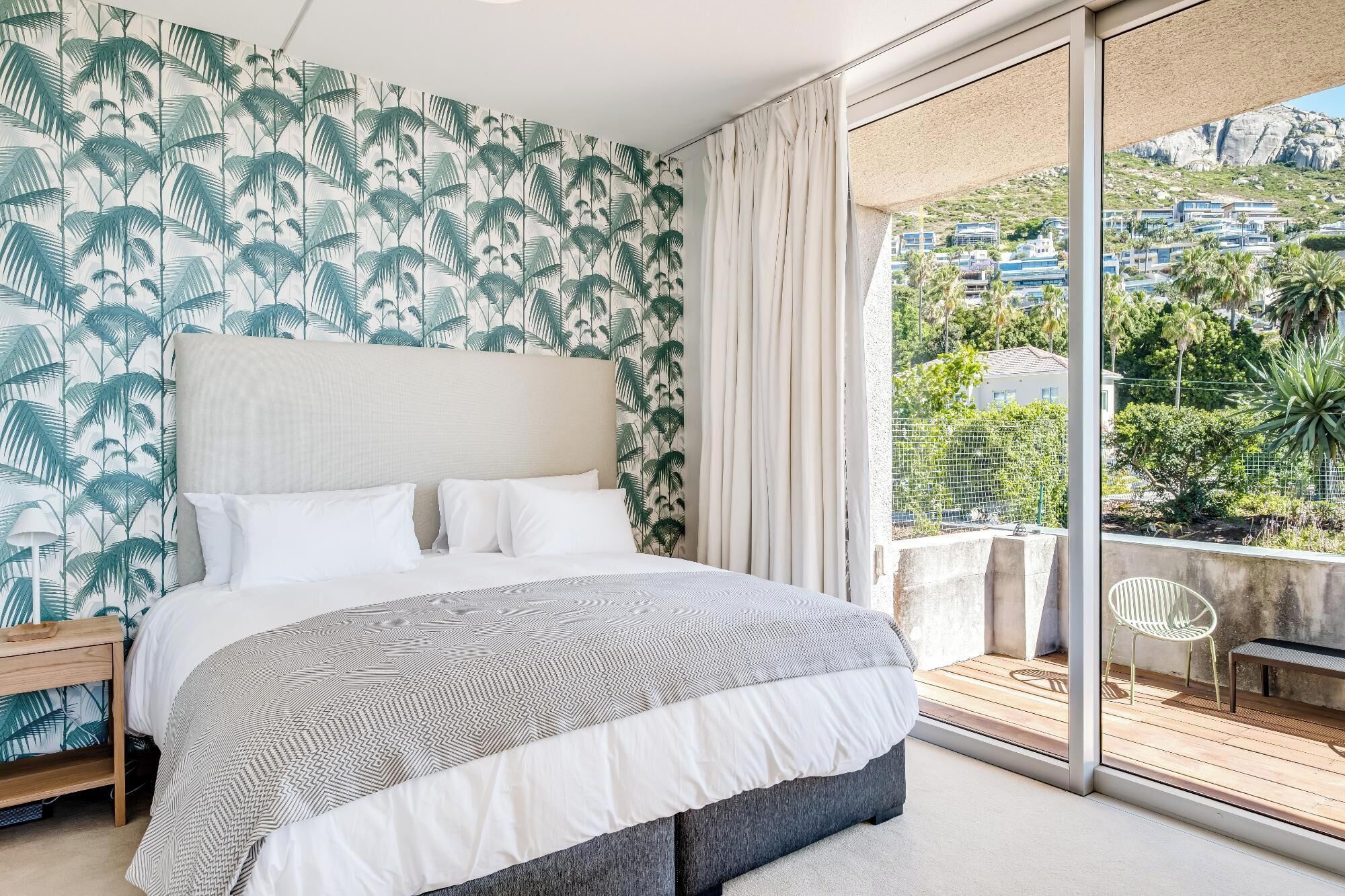 A bedroom with a large bed, a view of a balcony, and tropical wallpaper.