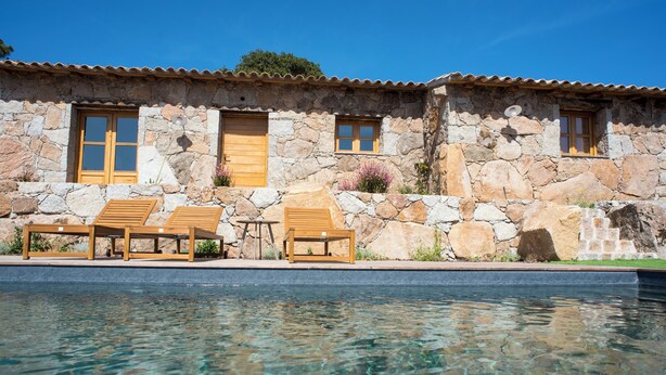Edifici de pedra amb piscina, portes i finestres de fusta.