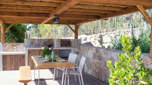 Terrassa exterior amb taula i cadires de fusta, mur de pedra i zona de barbacoa.