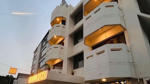A multi-story hotel with a prominent 'HOTEL 7CR' sign, featuring balconies on each floor and a central entrance with potted plants.