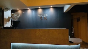 A hotel reception area with a dark blue wall, a reception desk, a seating area, and a ceiling fan.