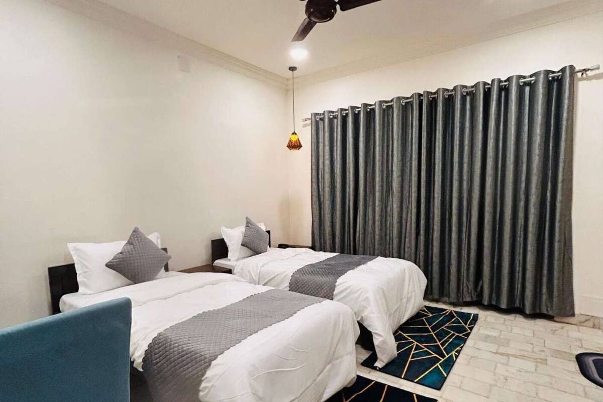 A hotel room with two beds, a ceiling fan, a hanging light, and a large window with curtains.