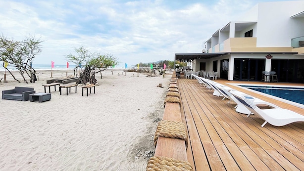 A beachside hotel with a wooden deck, lounge chairs, and a pool.