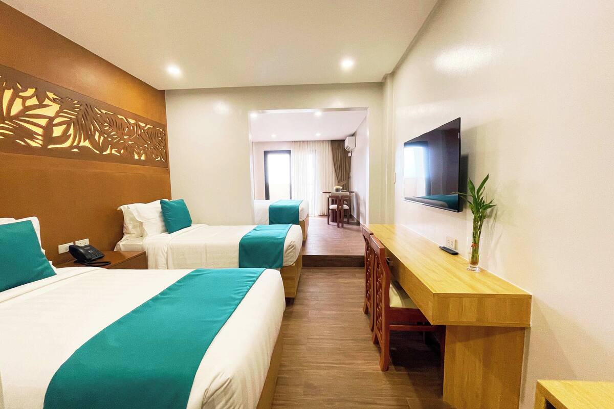 A hotel room with two beds, a desk, and a TV.