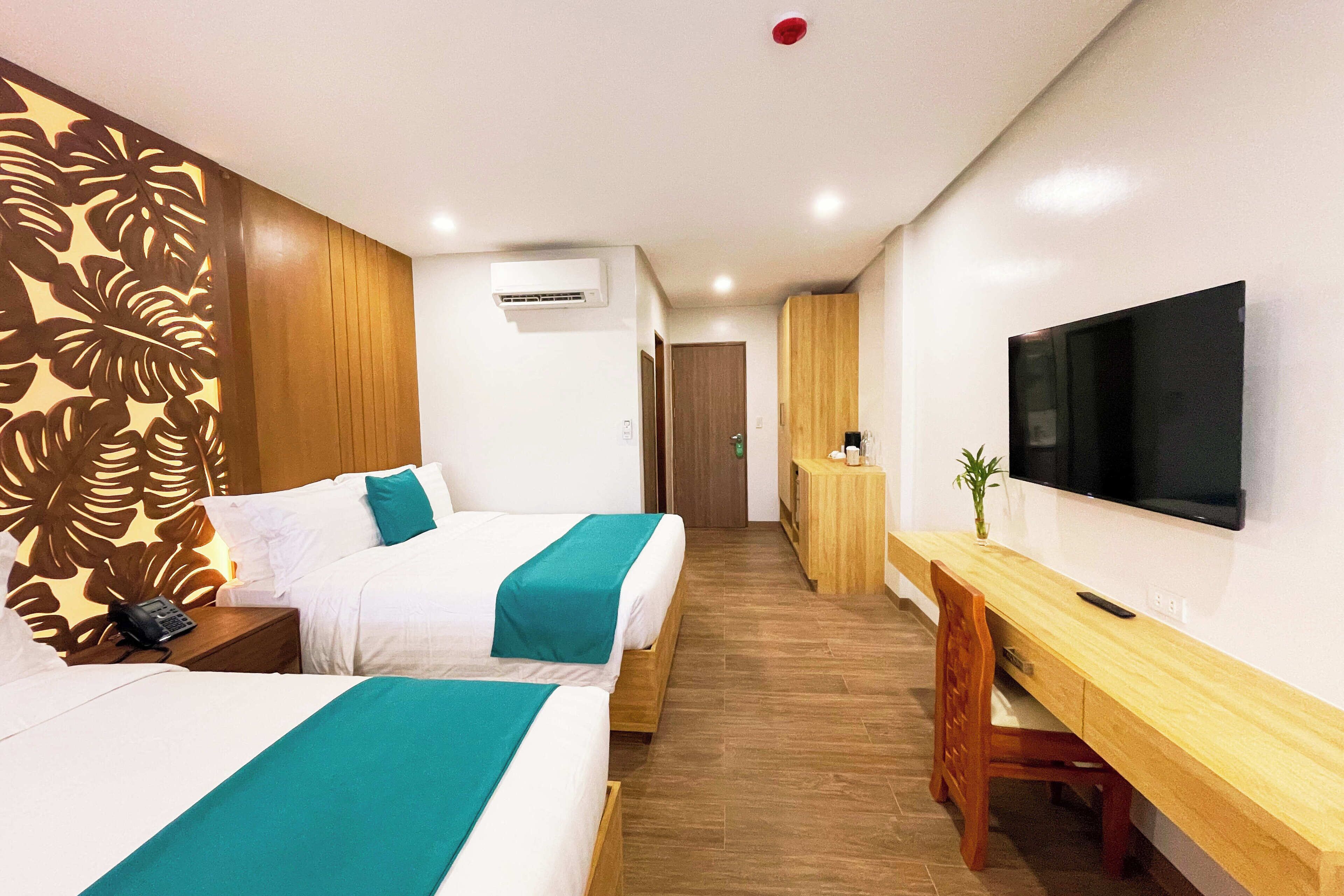 A hotel room with two beds, a wooden desk, a TV, and a wall-mounted air conditioner.