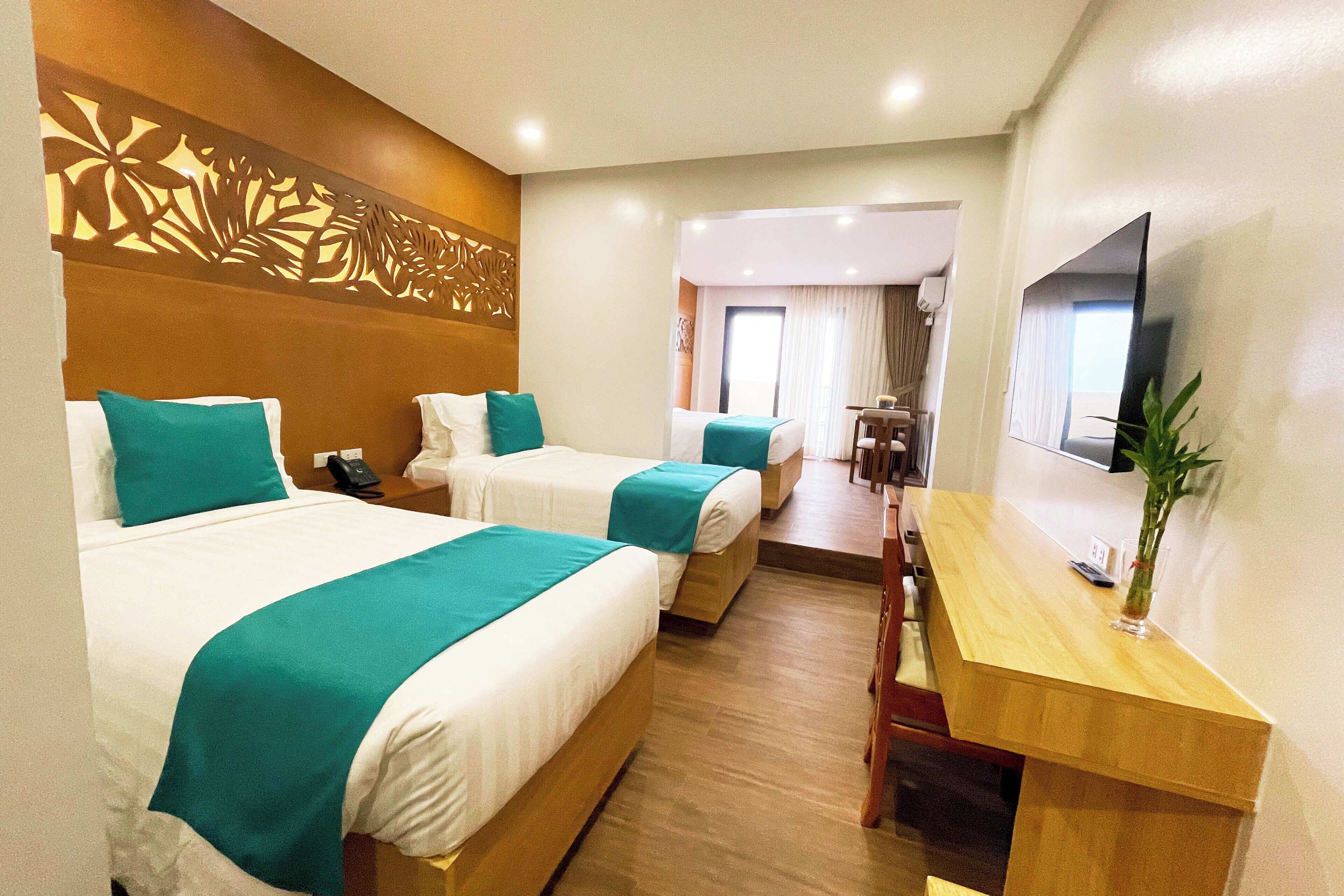 A hotel room with two beds, a desk, a TV, and a decorative wall panel.
