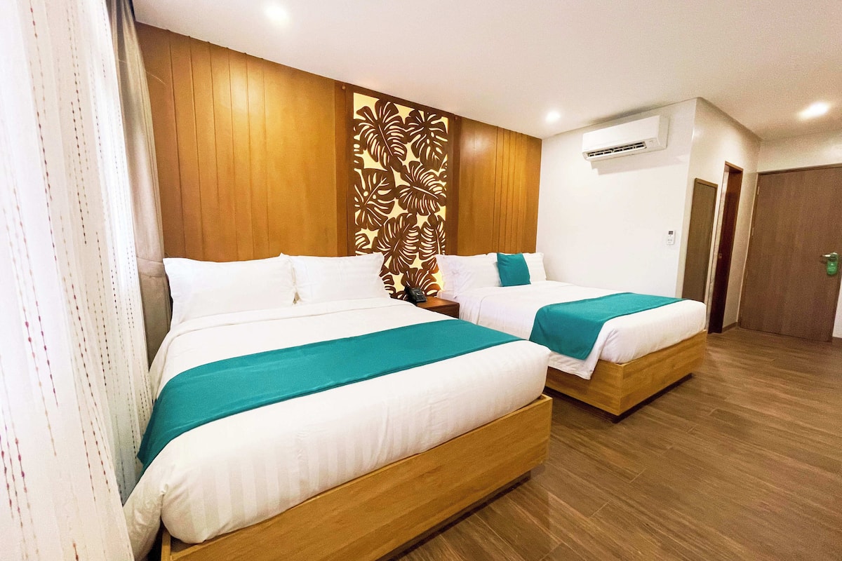 A hotel room with two beds, wooden headboard panels, a decorative wall panel, and an air conditioning unit.