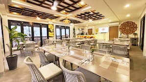 A dining area with multiple tables and chairs, a bar area, and large windows providing natural light.