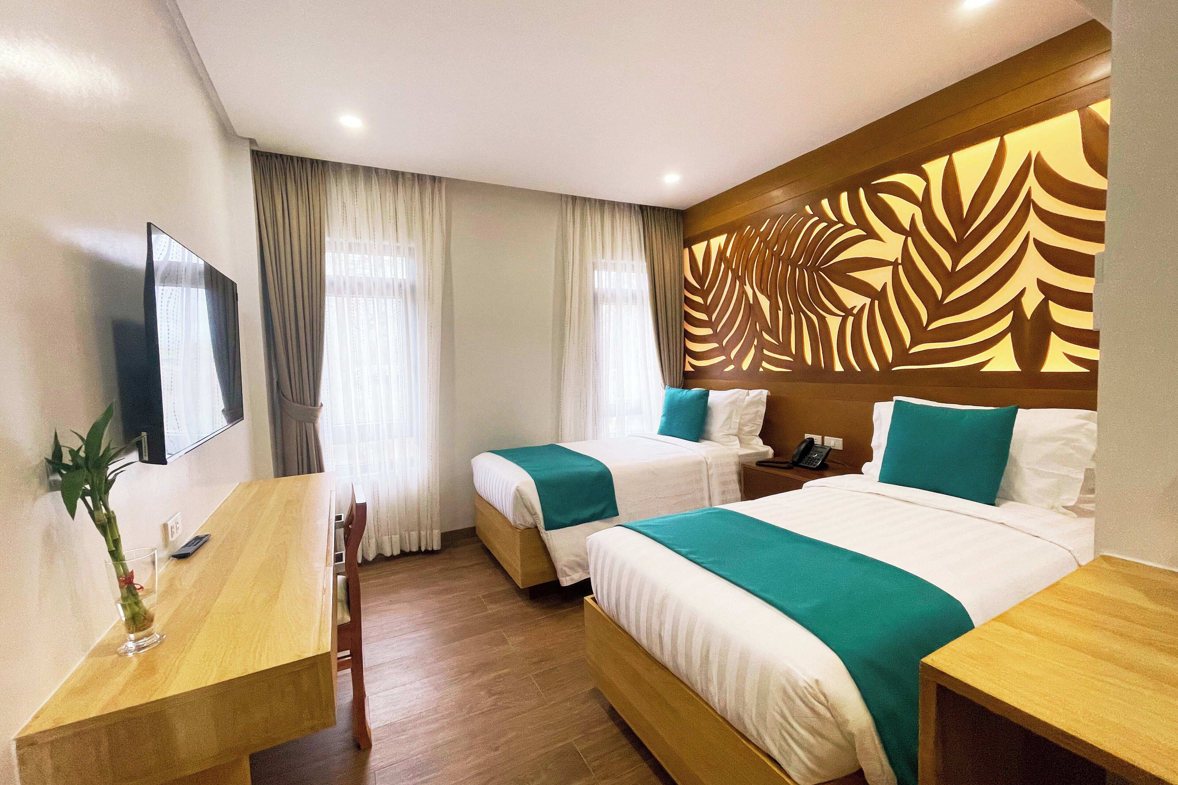 A hotel room with two beds, a wooden desk, a TV, and a decorative wall panel.