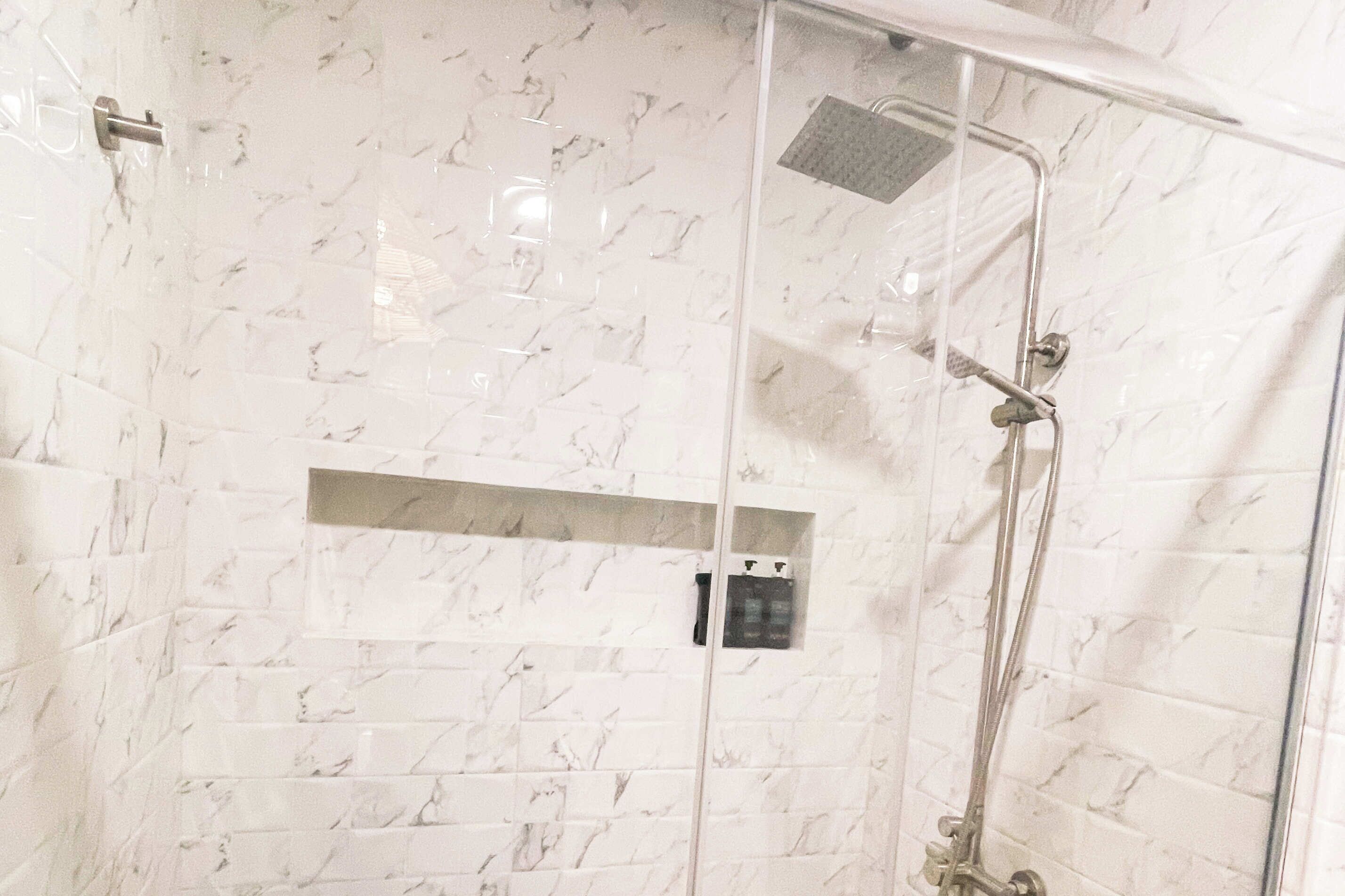 A glass-enclosed shower with a marble-tiled wall, a handheld showerhead, and a control panel.