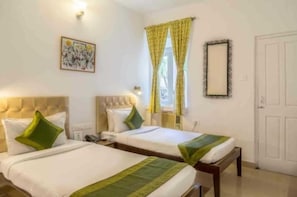 A hotel room with two beds, a bedside table, a mirror, and a window with curtains. - Mayfair Hotel Panjim (Panaji)