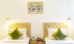 A hotel room with two beds, each with a tufted headboard and a green pillow. There is a framed artwork on the wall above the beds. - Mayfair Hotel Panjim (Panaji)