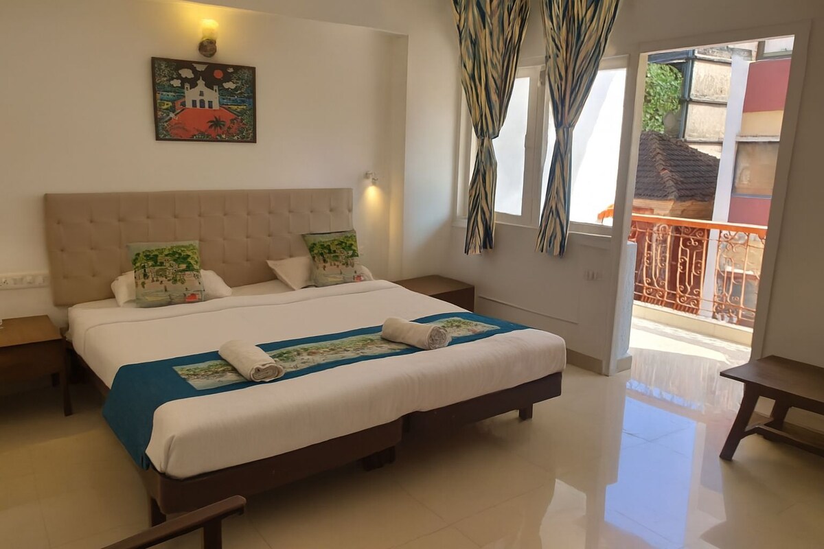 A hotel room with a large bed, two bedside tables, a painting on the wall, and a view of the outside balcony.