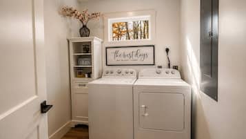 A laundry room with a washing machine, dryer, and a shelf with storage items.