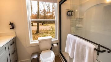 A bathroom with a toilet, a glass shower enclosure, a window with a view of trees, and a towel rack.