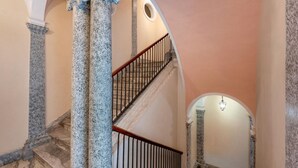 A grand staircase with marble columns and a wooden railing, leading to an upper floor. - GuestHost - Charming and cozy 91 square meters apartment, perfect for four people, located on the first floor of the historic Palazzo Auteri Perrotta (NO elevator).Elegantly decorated, it features two frescoed ceilings.The property is located in the hear (Catania)
