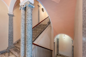 Una imponente escalera con columnas de mármol y barandilla de madera, que conduce a un piso superior.