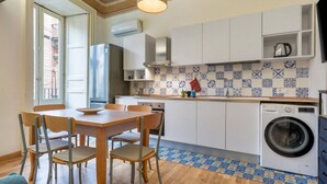 A compact kitchen with a dining area, a washing machine, and a tiled backsplash. - GuestHost - Charming and cozy 91 square meters apartment, perfect for four people, located on the first floor of the historic Palazzo Auteri Perrotta (NO elevator).Elegantly decorated, it features two frescoed ceilings.The property is located in the hear (Catania)