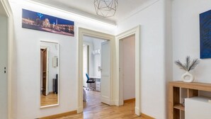A hallway with wooden flooring, white walls, and a cityscape painting. There is a desk with a chair in the background. - GuestHost - Charming and cozy 91 square meters apartment, perfect for four people, located on the first floor of the historic Palazzo Auteri Perrotta (NO elevator).Elegantly decorated, it features two frescoed ceilings.The property is located in the hear (Catania)