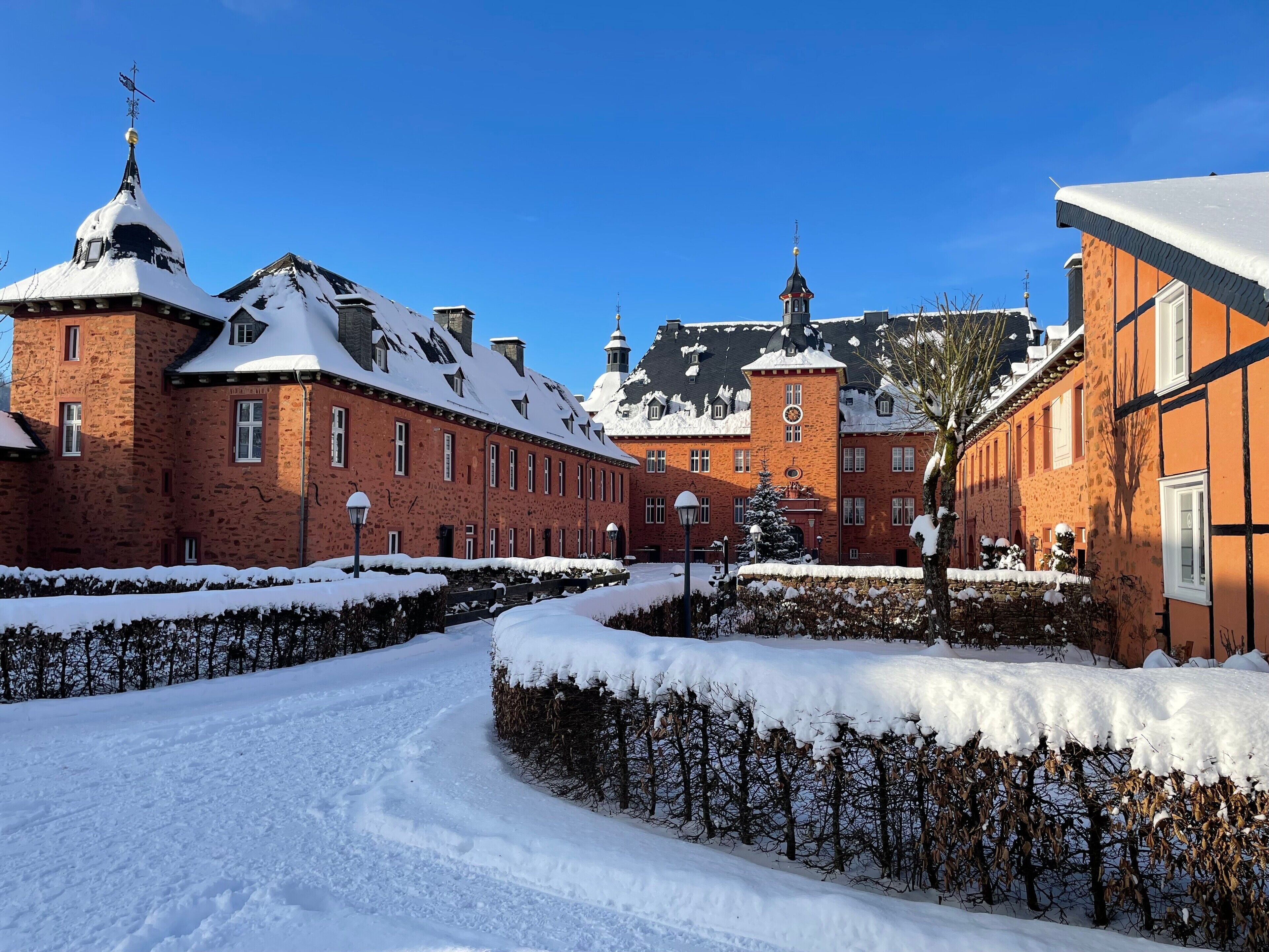 Un patio cubierto de nieve con edificios de ladrillo, cielo despejado y una colina distante.