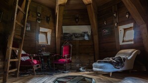 Interior rústico de una cabaña de troncos con vigas de madera, una silla roja, un sillón blanco y un cuadro en la pared.