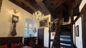 Una habitación con una escalera de madera, una mesa de comedor con cojines rojos, una araña y un reloj en la pared.