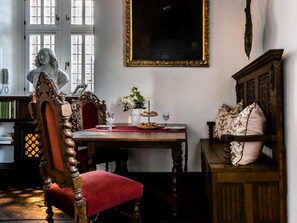 A room with a wooden chair, a table with a vase of flowers, a statue, and a framed painting.