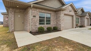 A two-story brick house with a beige front door, a garage, and a small front yard with trimmed bushes. - Relaxing 2BR Home w/ Contemporary Style (Madison)