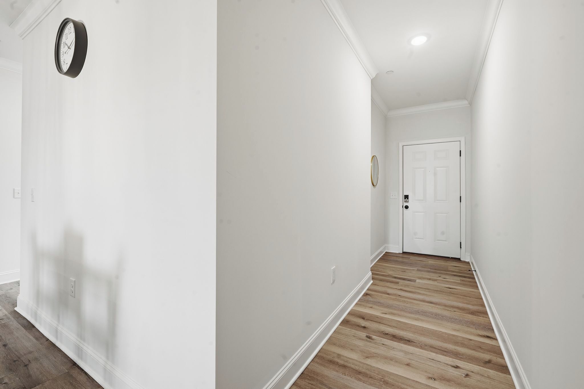 Un couloir aux murs blancs et au plancher en bois.