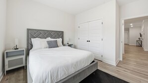 Ein Schlafzimmer mit Bett, Nachttischen, einem Kleiderschrank und einer Tür zu einem anderen Raum.