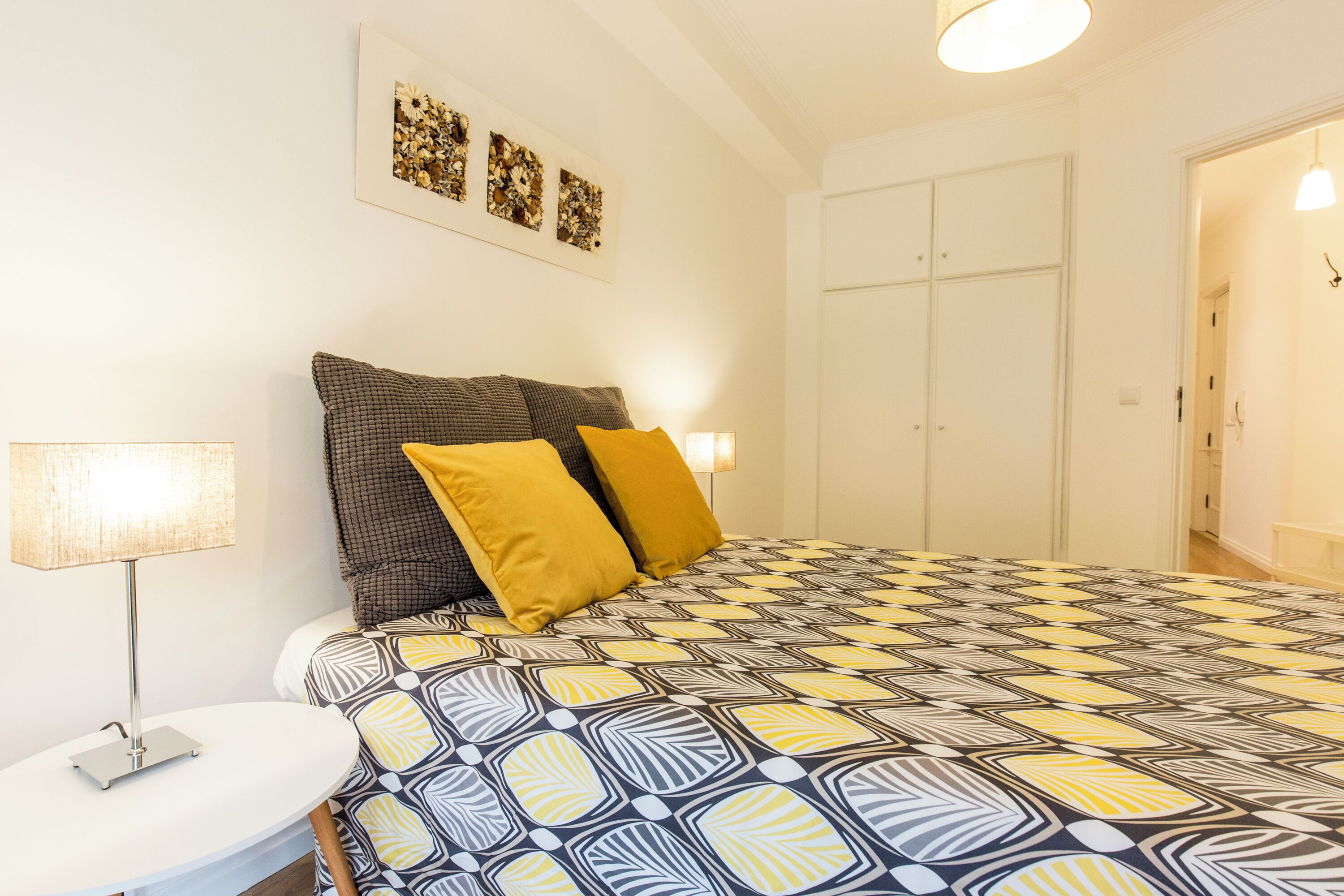 Una camera da letto con una coperta a motivi, una lampada da comodino e un'opera d'arte appesa al muro.