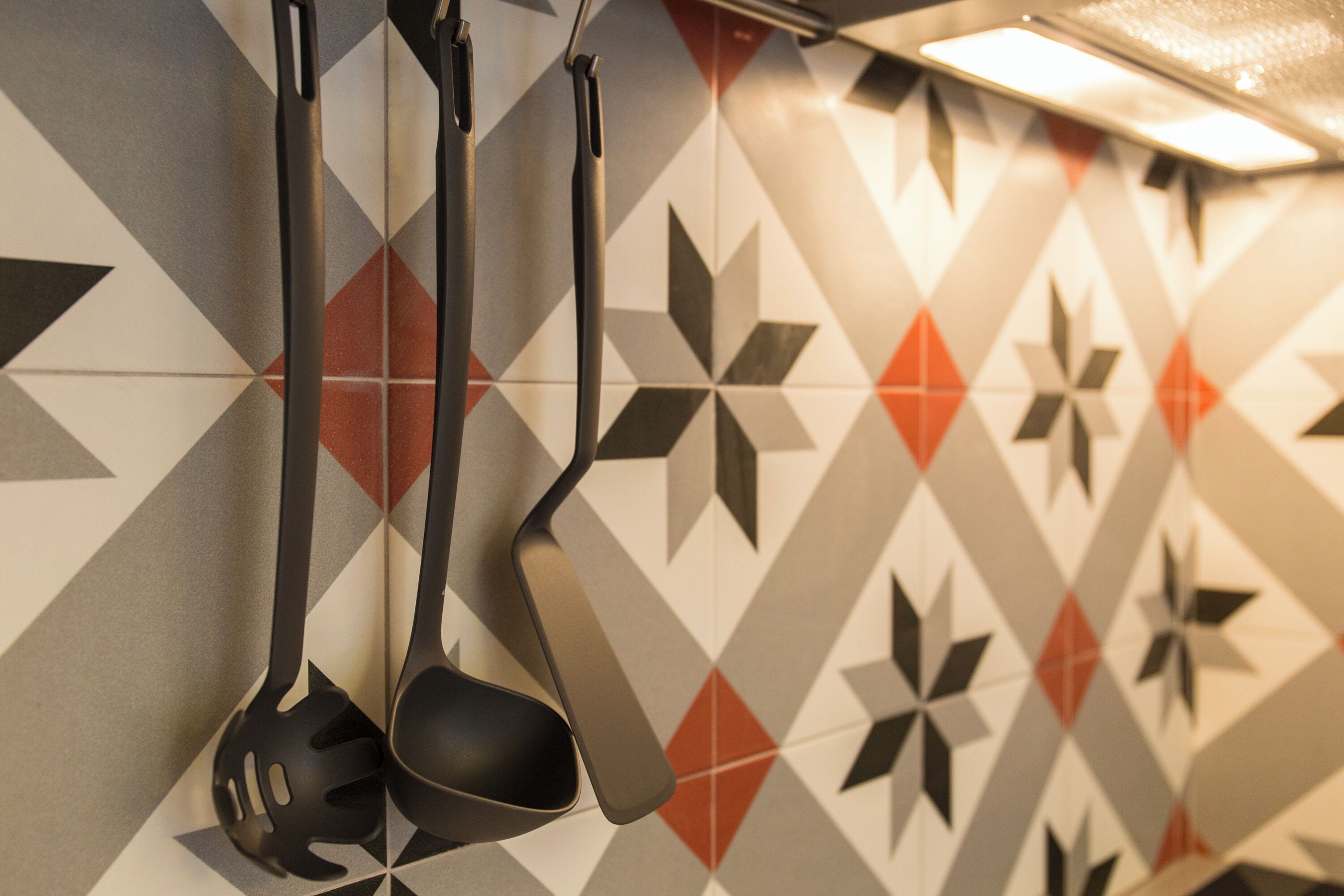 Una cocina con salpicadero de azulejos geométricos y utensilios de cocina negros colgados en la pared.