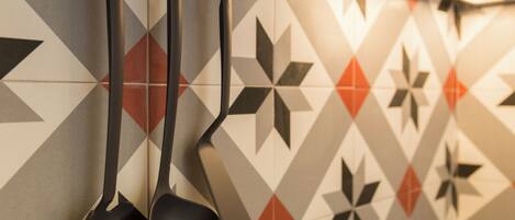 A kitchen with a geometric tile backsplash and black kitchen utensils hanging on the wall.