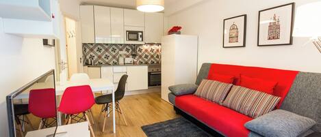 Un espacio habitable compacto con kitchenette, comedor y sofá con cojines rojos.