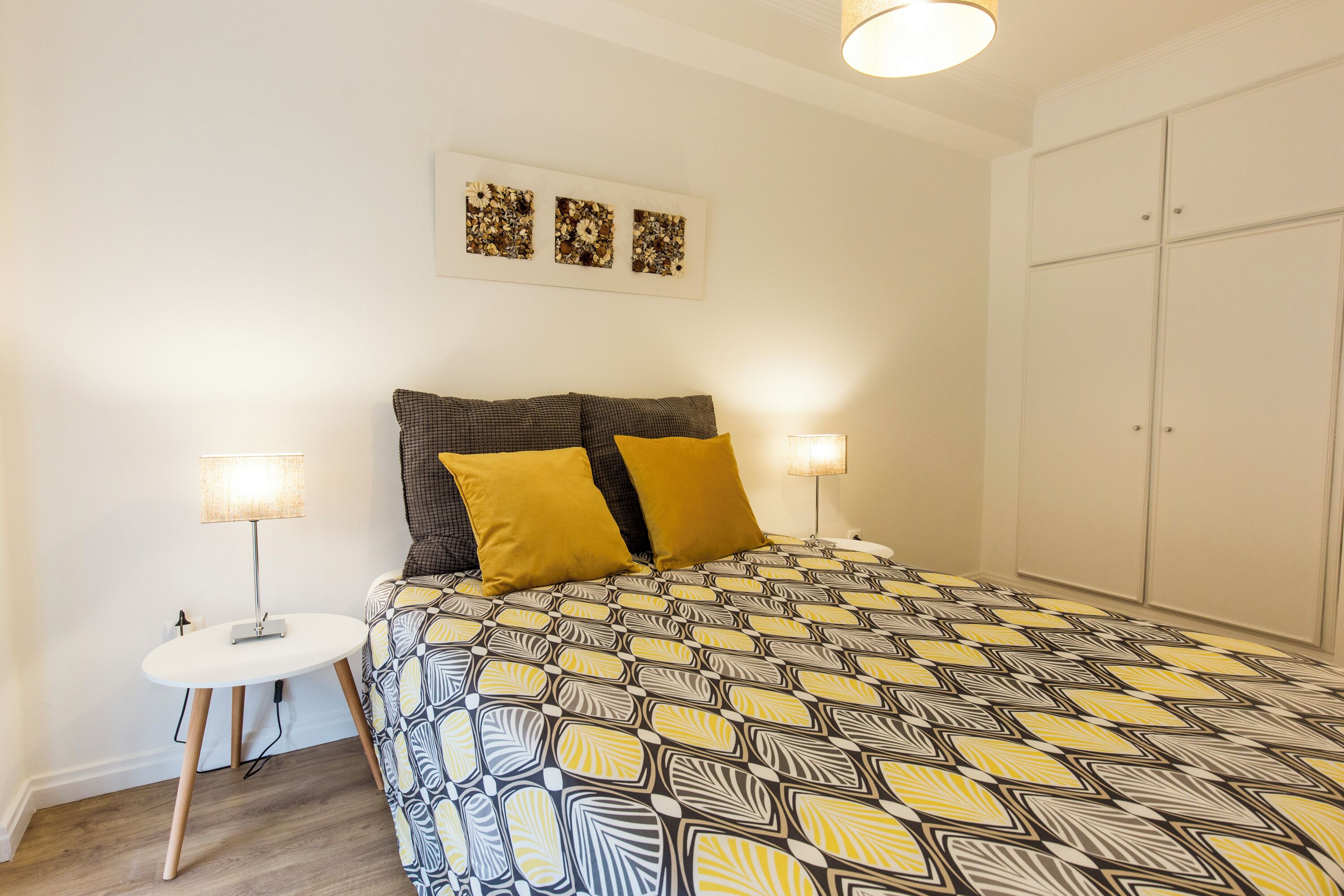 Une chambre à coucher avec une couvre-lit à motifs, deux lampes de chevet, une petite table ronde et une armoire.
