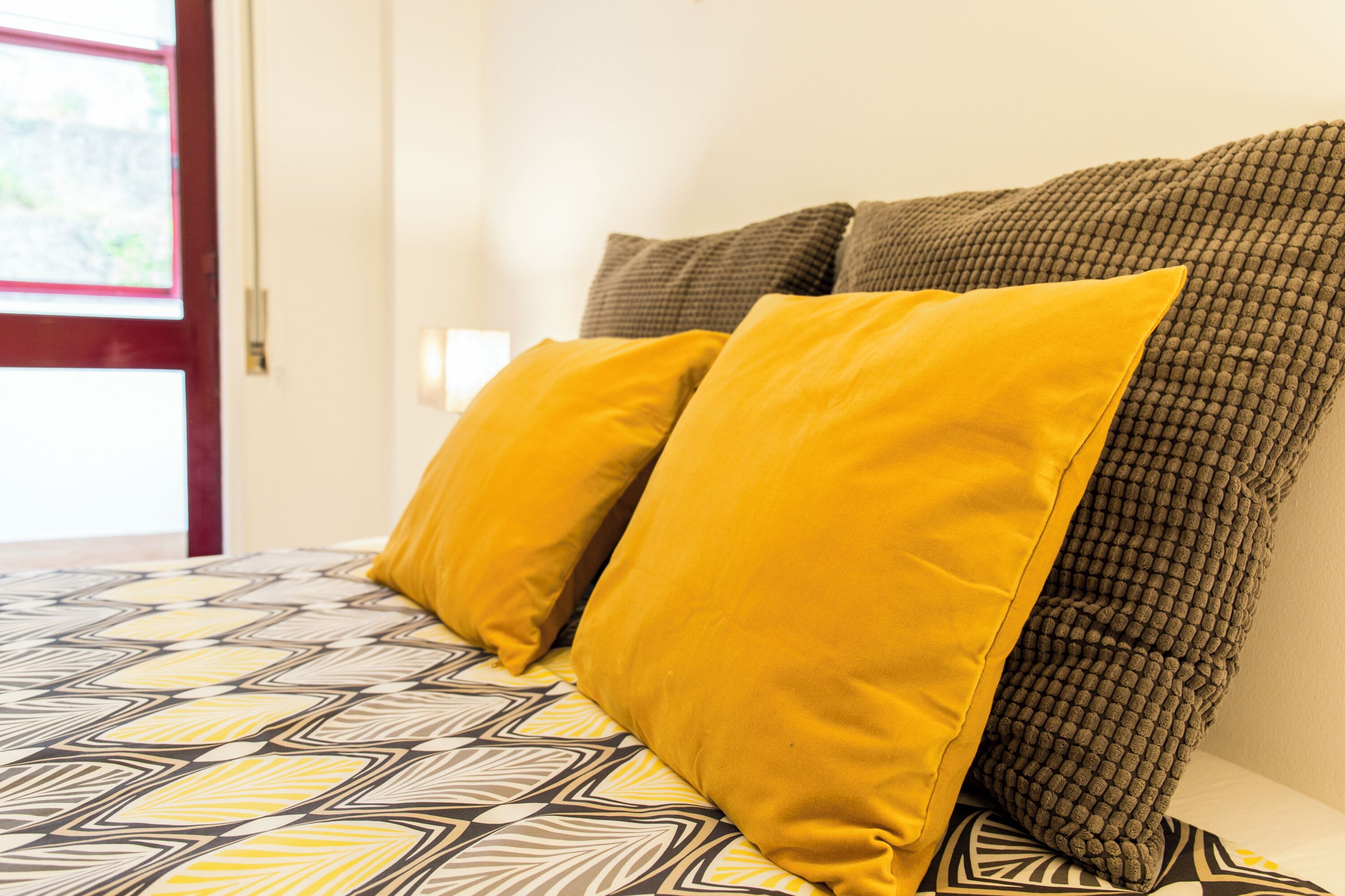 Un lit avec une couvre-lit à motifs et deux oreillers, un jaune et un marron.