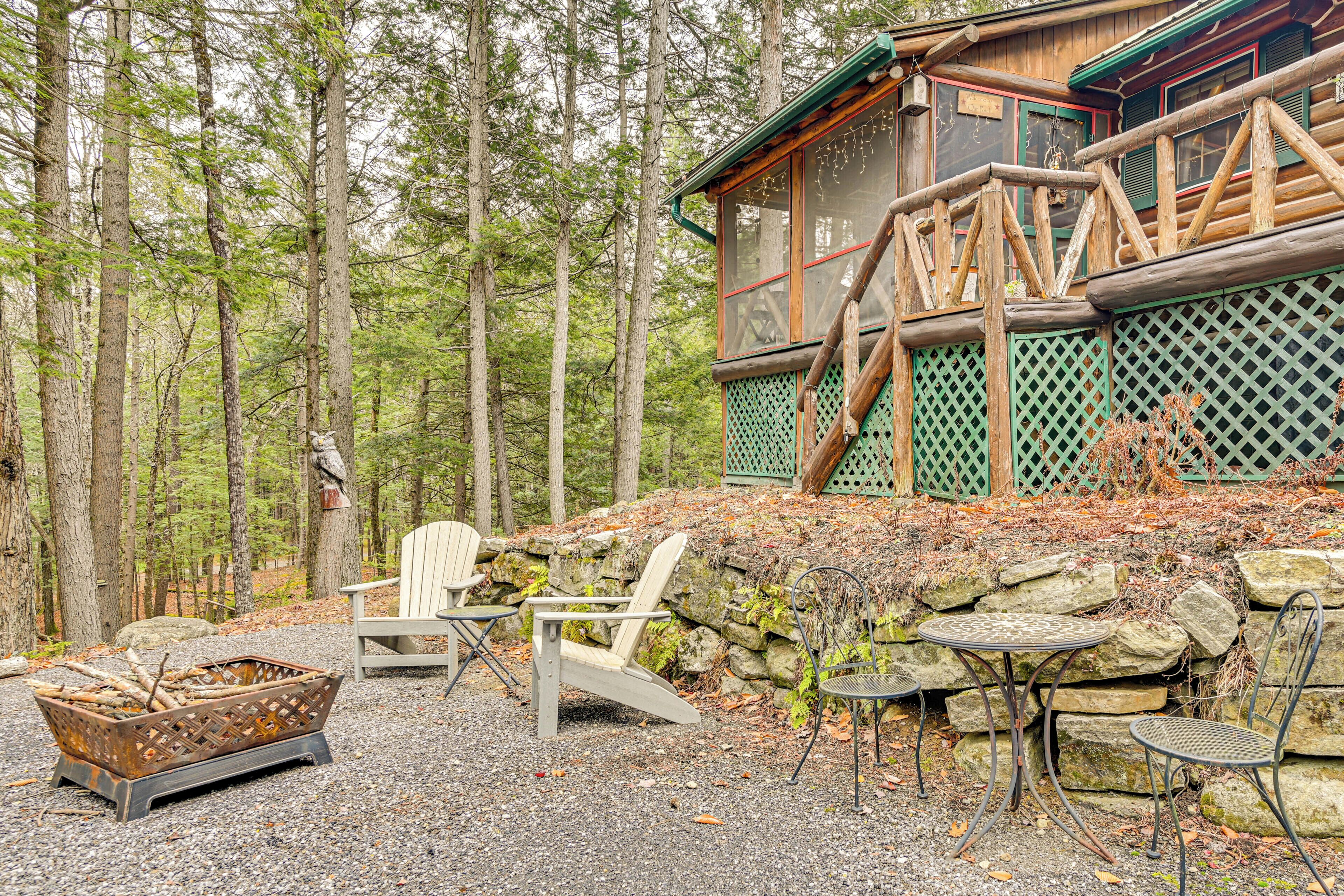 A rustic cabin with a stone wall, wooden deck, and a fire pit.