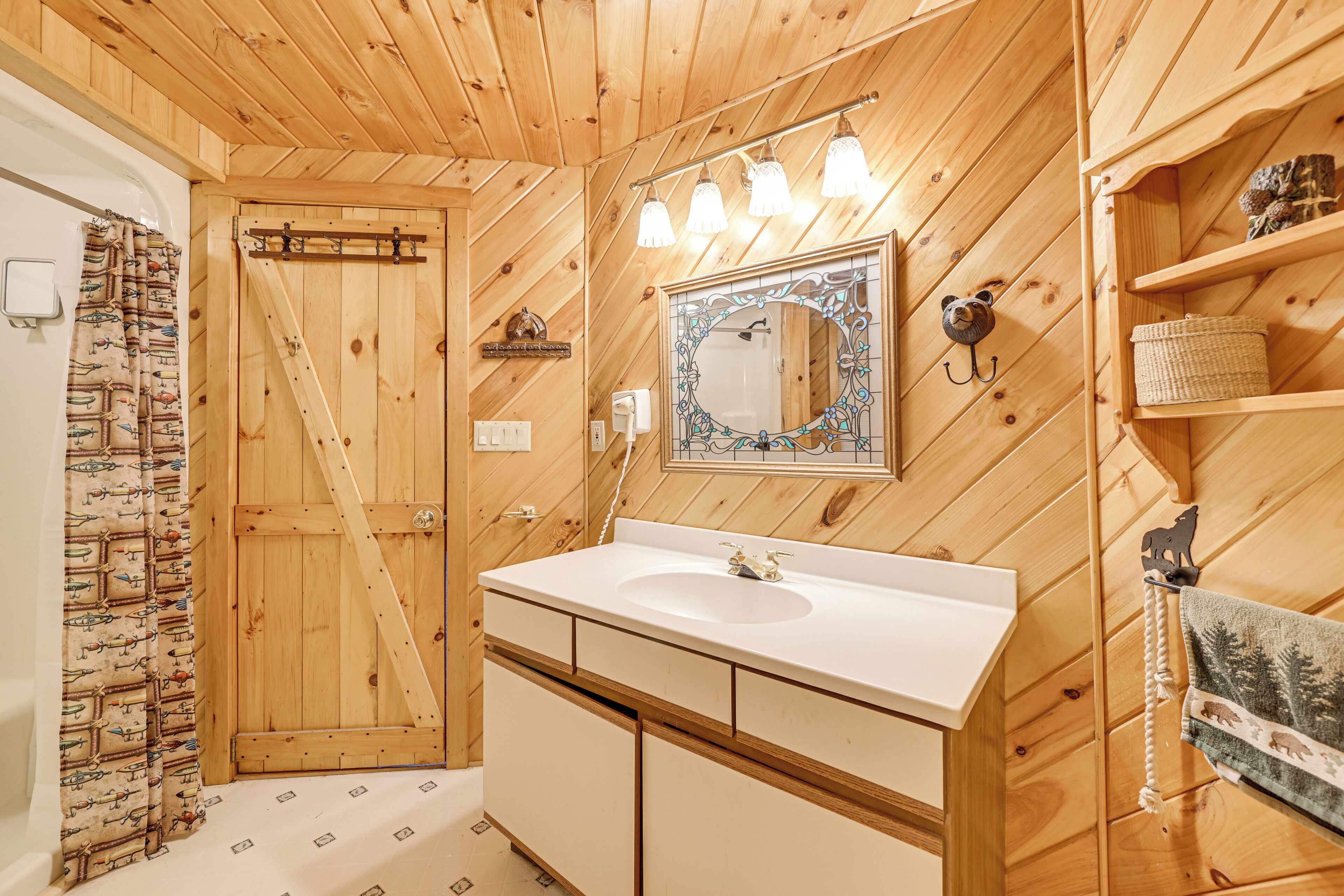 Une salle de bain aux murs lambrés, avec un lavabo blanc, un miroir doté d’un cadre orné et une porte en bois.