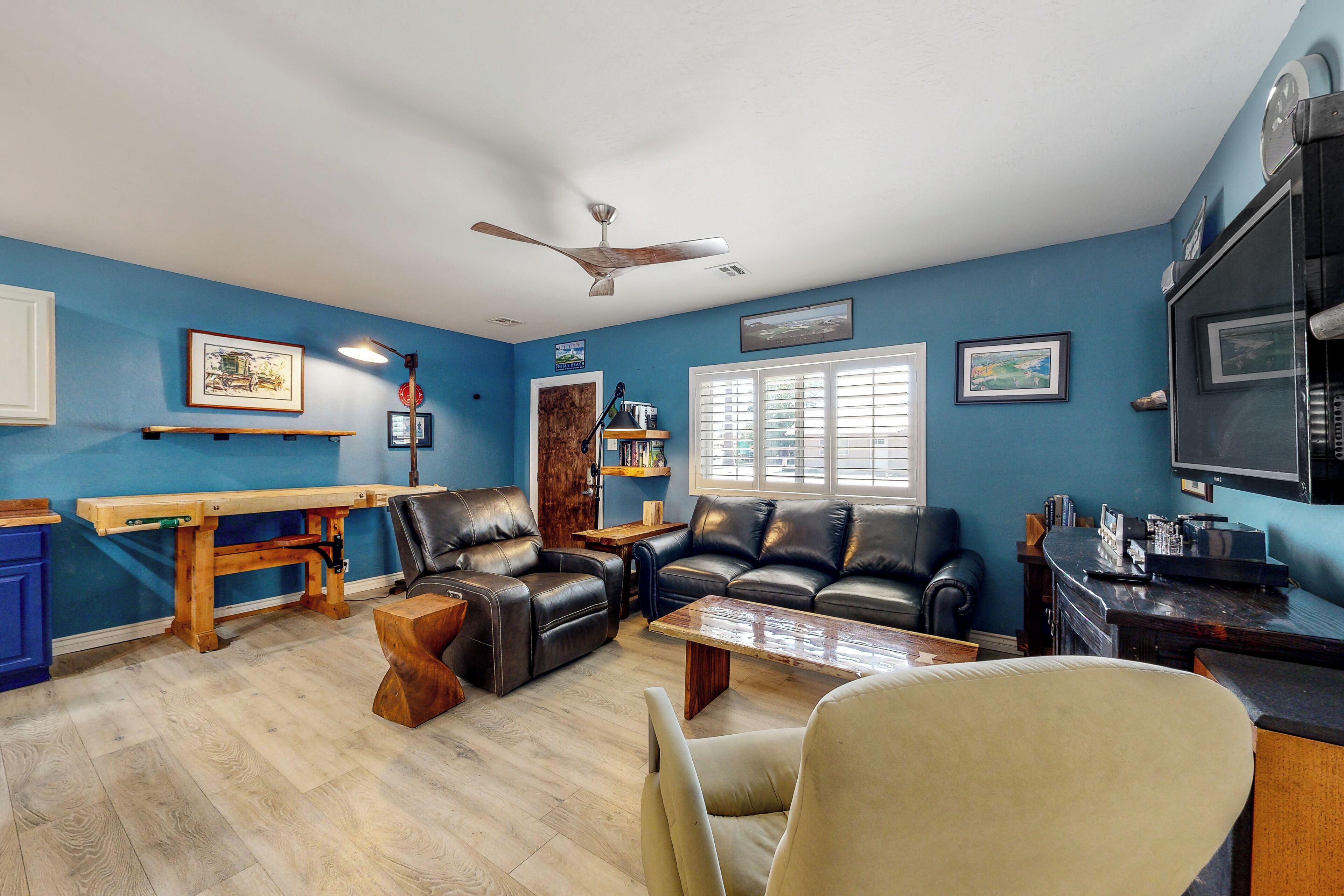 Un salon avec un mur bleu, un ventilateur de plafond, une table en bois, un canapé en cuir et un téléviseur.