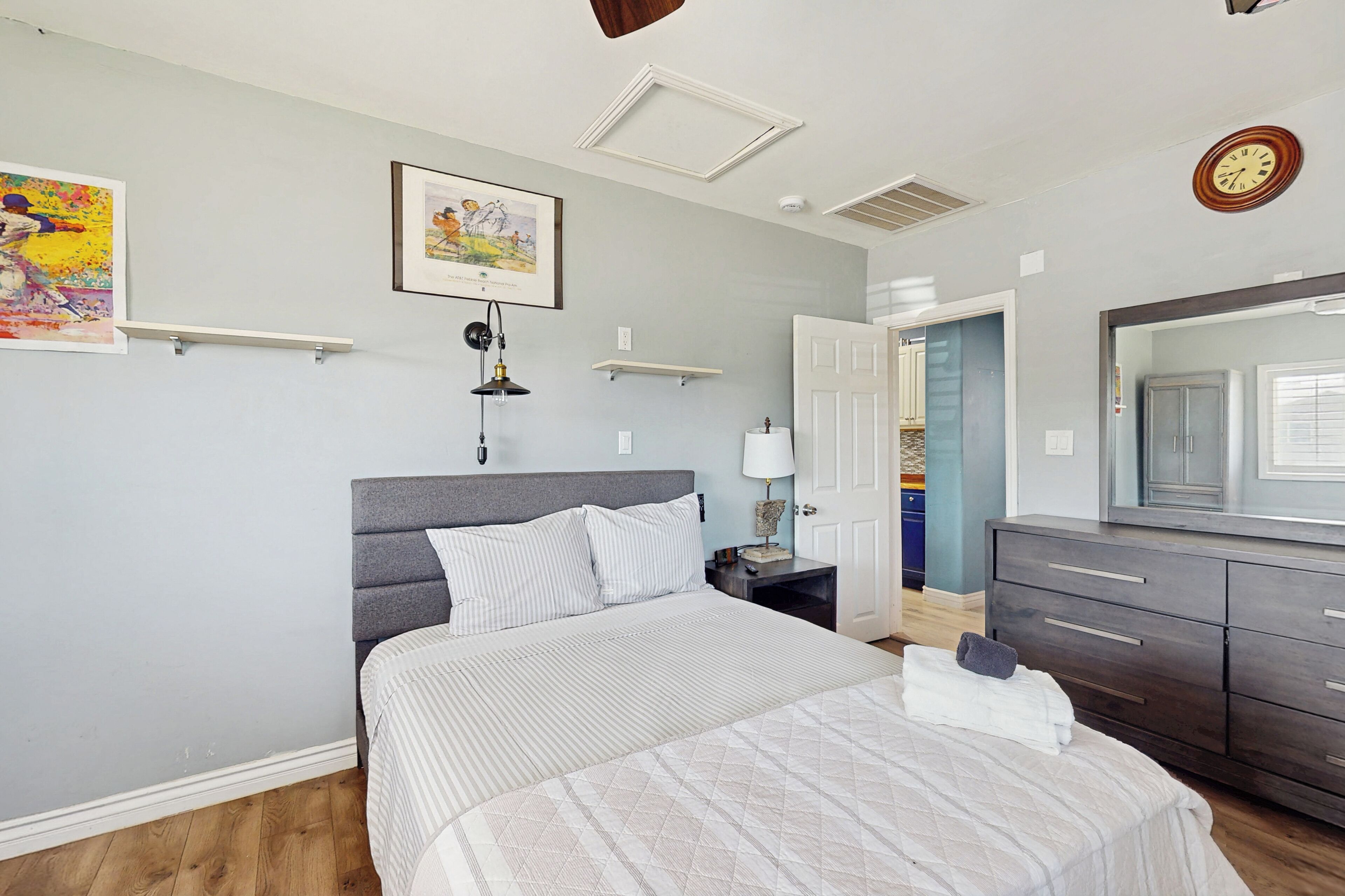 Ein Schlafzimmer mit einem Bett, Nachttischen, einer Lampe, einer Kommode und Bildern an den Wänden.