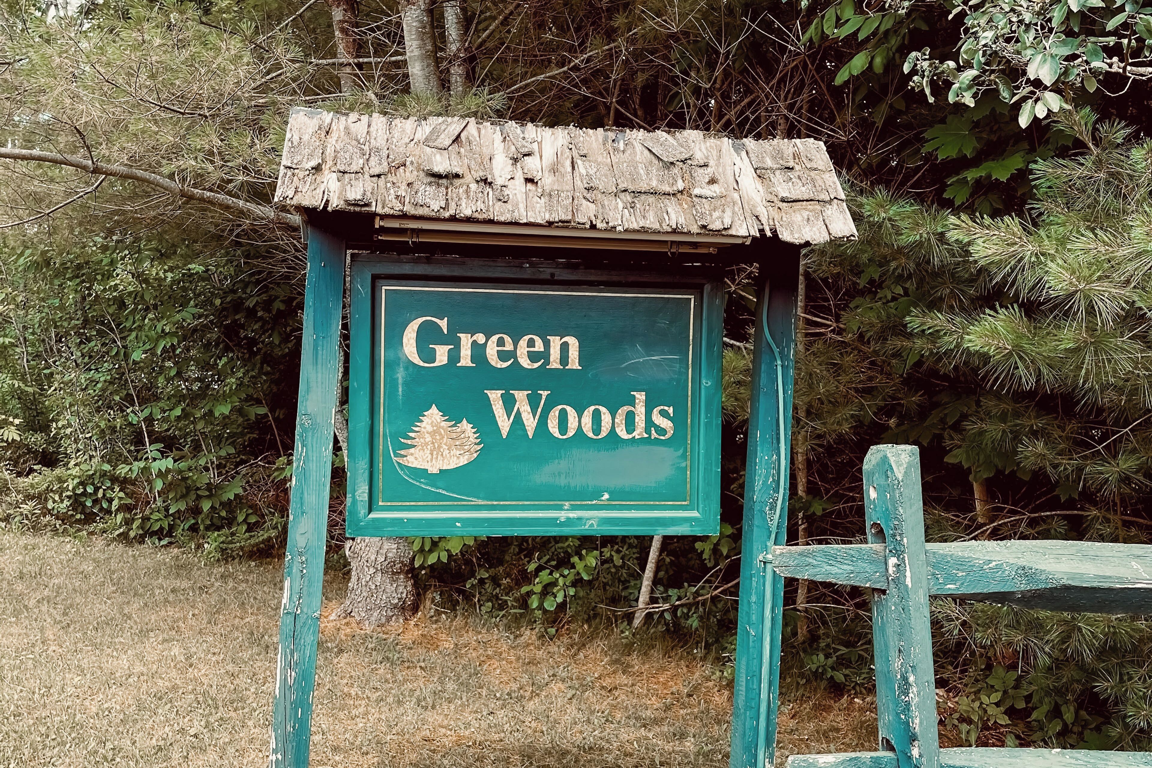 Een bord voor Green Woods, met een rustiek houten dak en een groene achtergrond.