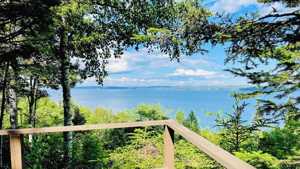 A wooden deck overlooking a forested area with a view of a lake and distant mountains. - Bay-view Getaway w/ Deck Between Camden & Belfast! (Lincolnville)